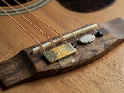 Macro detail of an acoustic instrument bridge with a brass sensor taped near the saddle