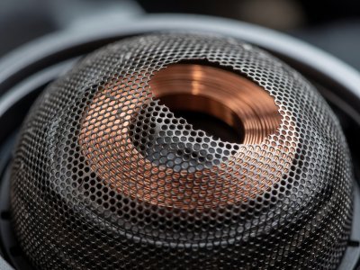 Macro view of an open-back headphone copper voice coil through perforated metal mesh